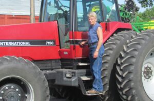 Marcia stands on the bottom step of the ladder on her red tractor.