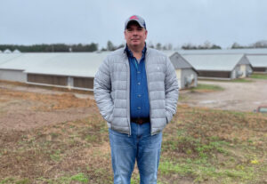 Marcus Milford stands in foreground with two poultry barns in the background.