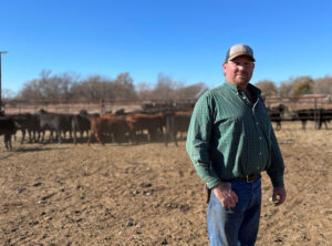 Chad Budy stands in foreground with a herd of cattle in the background.