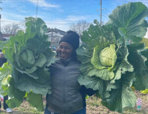 Renee Foster holding a large head of cabbage in each hand.