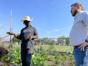 Coy Poitier shows off his urban farm. He stands to the left and talks to Stefen Tucker who stands on the right.
