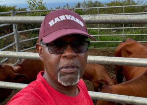 Royce Creque takes a selfie in front of a pen of cattle.