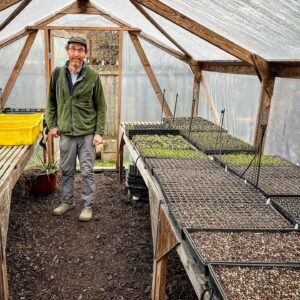 Josh Volk stands in his greenhouse with seedlings on tables